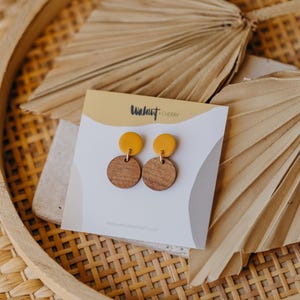 Puede incluir: Un par de pendientes de madera de color amarillo y marr&oacute;n. Los pendientes est&aacute;n sobre una tarjeta blanca con el texto "Walnut Cherry" impreso en ella.