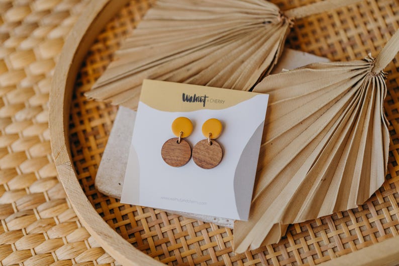 Puede incluir: Un par de pendientes de madera de color amarillo y marr&oacute;n. Los pendientes est&aacute;n sobre una tarjeta blanca con el texto "Walnut Cherry" impreso en ella.