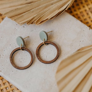 May include: A pair of wooden hoop earrings with a light green circle attached to the top of each hoop.