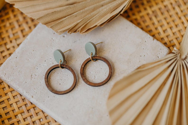 May include: A pair of wooden hoop earrings with a light green circle attached to the top of each hoop.