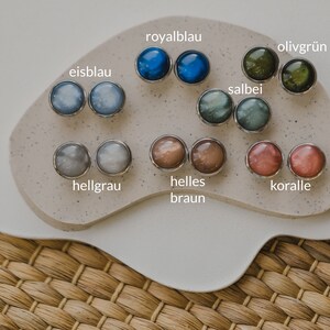 May include: A set of 10 pairs of earrings with different colors and patterns. The colors include ice blue, royal blue, sage, olive green, light gray, light brown, and coral. The earrings are displayed on a white surface.