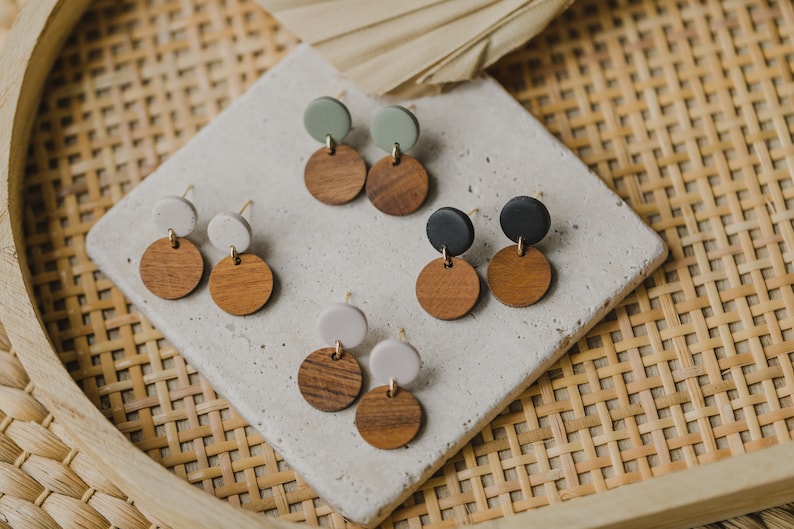 May include: Three pairs of earrings with wooden and clay circles. The earrings are in shades of green, white, and black.