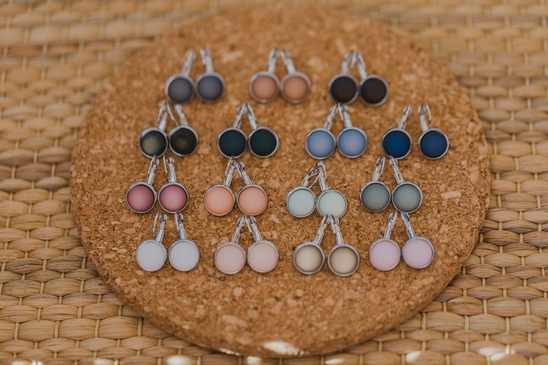 May include: A set of 12 pairs of earrings with different colored glass cabochons. The earrings are silver-toned and have a leverback closure.