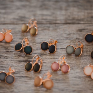 May include: Assortment of colorful round earrings with gold-tone hooks. The earrings are displayed on a wooden surface.