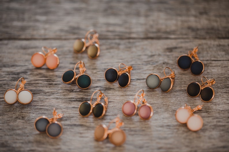 May include: Assortment of colorful round earrings with gold-tone hooks. The earrings are displayed on a wooden surface.