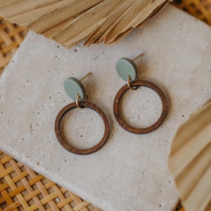May include: A pair of wooden hoop earrings with a green circle accent. The earrings are on a light gray surface.