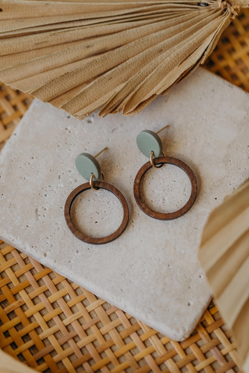 May include: A pair of wooden hoop earrings with a green circle accent. The earrings are on a light gray surface.
