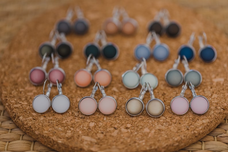 May include: A collection of 10 pairs of silver stud earrings with various colored glass cabochons. The colors include pink, peach, white, gray, blue, and green.