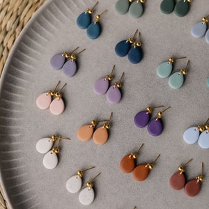 May include: A collection of 18 pairs of teardrop-shaped earrings in various colors, including blue, green, purple, pink, brown, gray, and white. The earrings are made of clay and have gold-colored posts.