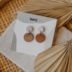 May include: A pair of earrings with a white and brown speckled design. The earrings are made of wood and have a gold-colored metal post. The earrings are on a white card with the text "Walnut & Cherry" printed on it.