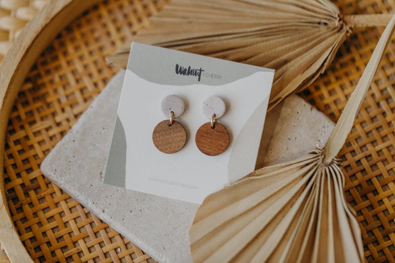 May include: A pair of earrings with a white and brown speckled design. The earrings are made of wood and have a gold-colored metal post. The earrings are on a white card with the text "Walnut & Cherry" printed on it.