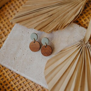 May include: A pair of earrings featuring a light green and dark brown colour scheme. The earrings are crafted from wood and have a simple, minimalist design.