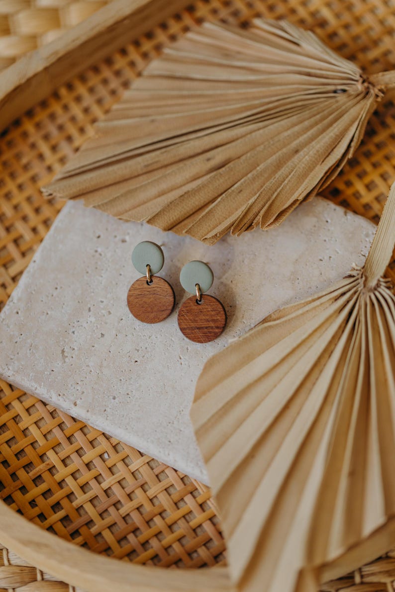 May include: A pair of earrings featuring a light green and dark brown colour scheme. The earrings are crafted from wood and have a simple, minimalist design.