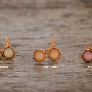 May include: Three pairs of earrings with different colored cabochons. The earrings are gold-toned and have a simple design. The colors are champagne, brown-taupe, and mauve.