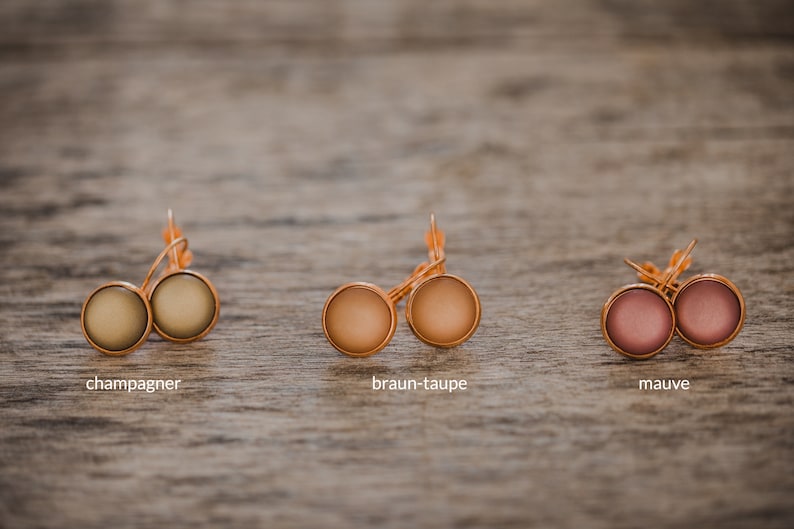 May include: Three pairs of earrings with different colored cabochons. The earrings are gold-toned and have a simple design. The colors are champagne, brown-taupe, and mauve.