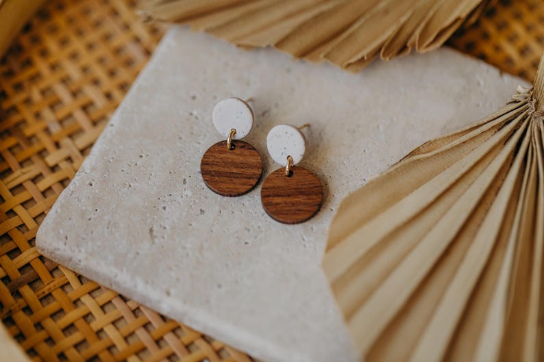 May include: A pair of earrings with white and brown round wooden discs. The earrings are on a light gray surface.
