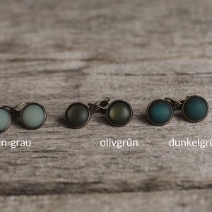 May include: Six pairs of earrings with different coloured glass cabochons. The colours are green-grey, olive green, and dark green/petrol.