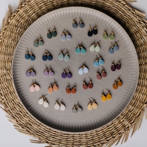 May include: A collection of 24 pairs of small, teardrop-shaped clay earrings in various colors, displayed on a gray plate. The earrings are arranged in rows and are all the same size and shape.