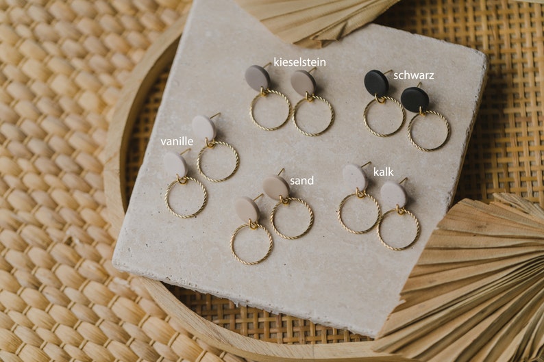 May include: Six pairs of gold hoop earrings with different colored clay discs. The colors are: vanille, kieselstein, schwarz, kalk, sand.