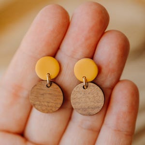 Puede incluir: Un par de pendientes con un c&iacute;rculo amarillo encima de un c&iacute;rculo de madera marr&oacute;n.