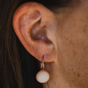 May include: A pair of rose gold earrings with a white round stone pendant.