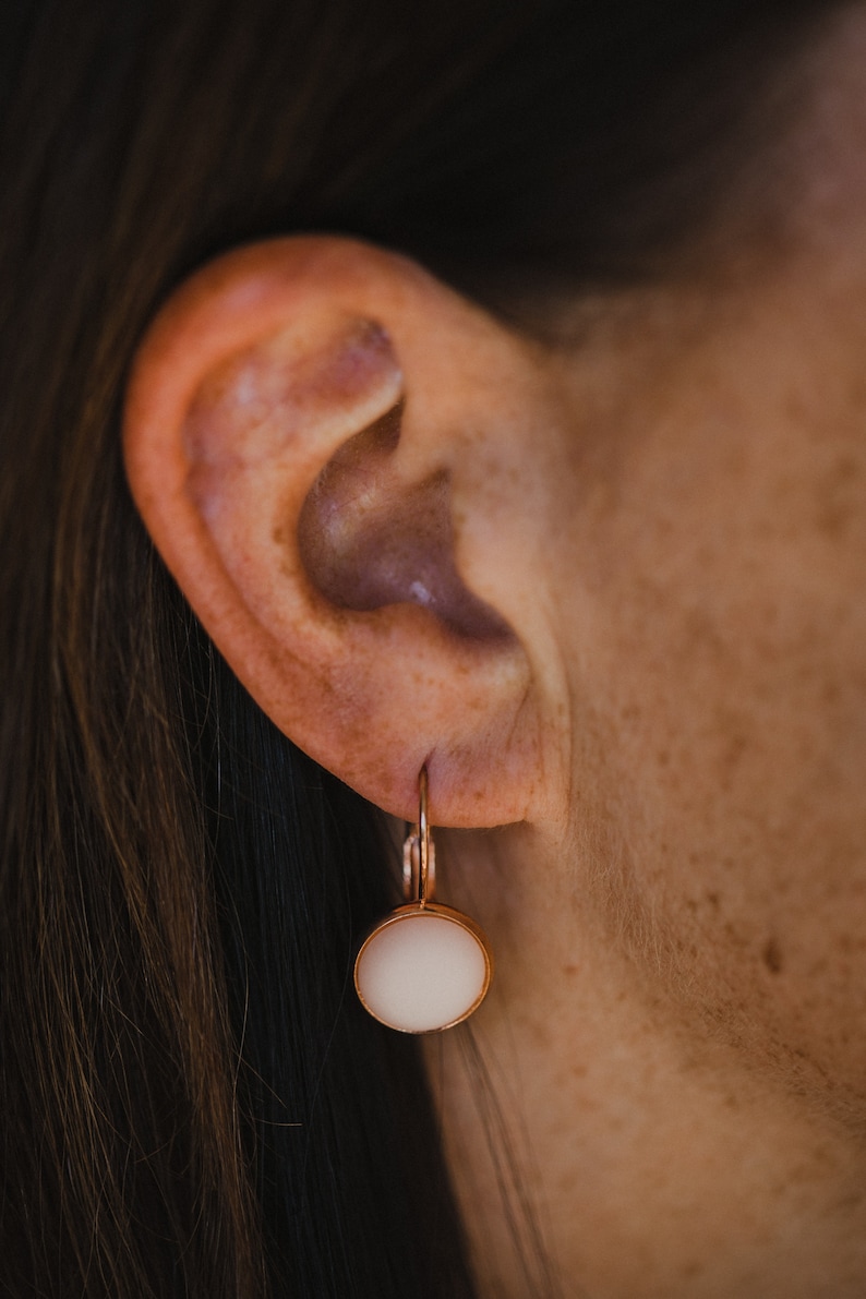 May include: A pair of rose gold earrings with a white round stone pendant.
