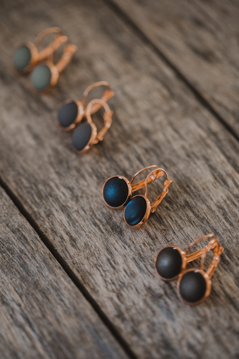 May include: Four pairs of hoop earrings with different colored stones. The earrings are on a wooden surface. The stones are black, green, and blue.