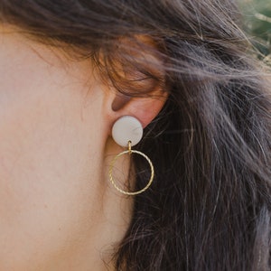 May include: A pair of earrings with a white ceramic disc and a gold hoop.
