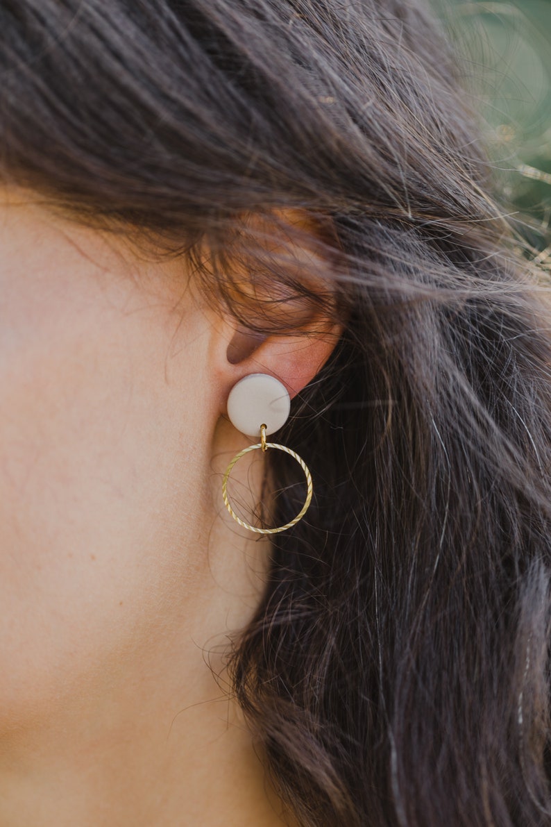 May include: A pair of earrings with a white ceramic disc and a gold hoop.