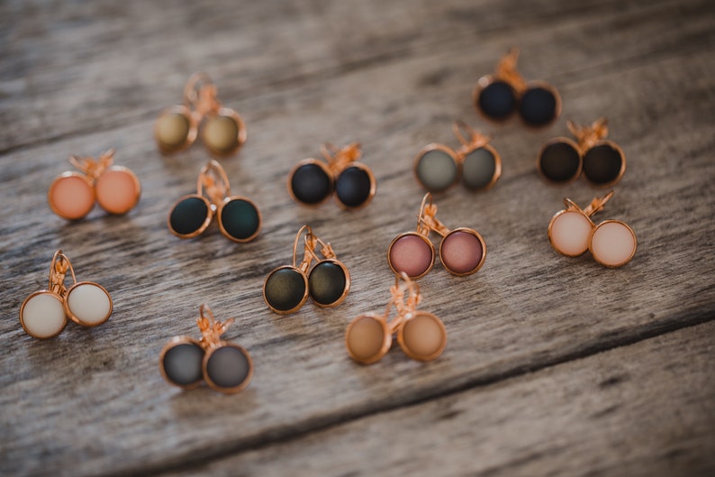 May include: A collection of 10 pairs of earrings with different colored glass cabochons. The earrings are made with gold-toned metal and have a leverback closure.