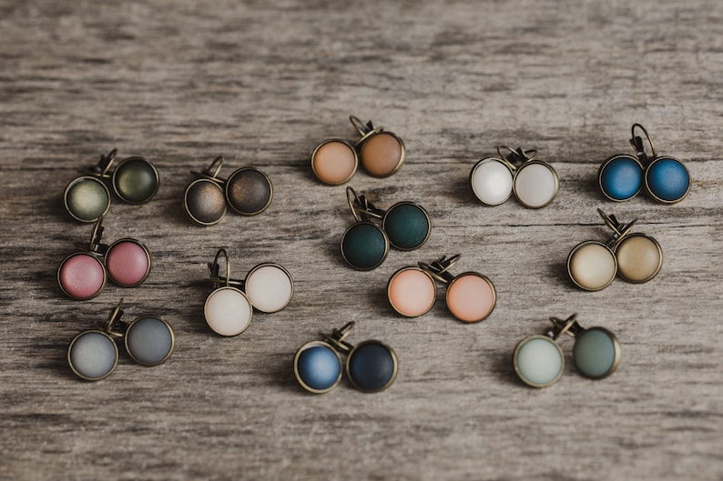 May include: Assortment of 10 pairs of earrings with various colours and finishes. The earrings are displayed on a wooden surface. The colours include green, brown, pink, white, blue, and beige.