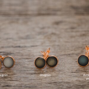 May include: Three pairs of earrings with different colored glass cabochons. The earrings are silver with a hook closure. The colors are gray-green, olive green, and dark green/petrol.