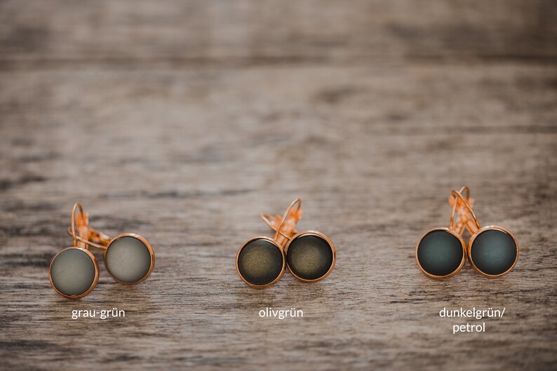 May include: Three pairs of earrings with different colored glass cabochons. The earrings are silver with a hook closure. The colors are gray-green, olive green, and dark green/petrol.