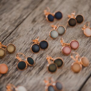 May include: Assortment of 10 pairs of earrings with various colors and finishes. The earrings are made of metal and have a round shape. The colors include black, gray, green, brown, pink, and white.