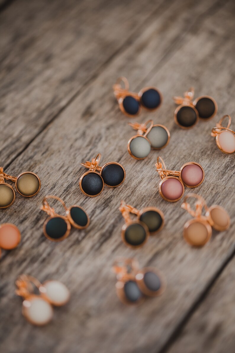 May include: Assortment of 10 pairs of earrings with various colors and finishes. The earrings are made of metal and have a round shape. The colors include black, gray, green, brown, pink, and white.