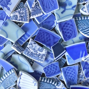 May include: A collection of broken ceramic shards featuring various blue and white patterns, including floral motifs, geometric lines, and textured pineapple-like designs, scattered together to form a mosaic of fragmented pottery pieces.