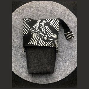 Może przedstawiać: Czarno-biała, wzorzysta kosmetyczka zapinana na zamek błyskawiczny z czarnym dnem z dżinsu. Kosmetyczka ma biały sznurek.