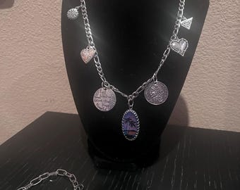Può includere: Una collana a catena d'argento con più ciondoli, tra cui un cuore, una palma e un ciondolo rotondo con il testo "Live, Breathe, Believe, Be Strong, Be Happy, Be Yourself". La collana è esposta su un manichino nero. Sono anche mostrati un braccialetto d'argento e due orecchini d'argento.