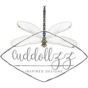 May include: A logo for a business called "cuddollzz inspired designs" featuring a stylized dragonfly with blue, green, yellow, and brown accents. The dragonfly is centered in a gray diamond shape.