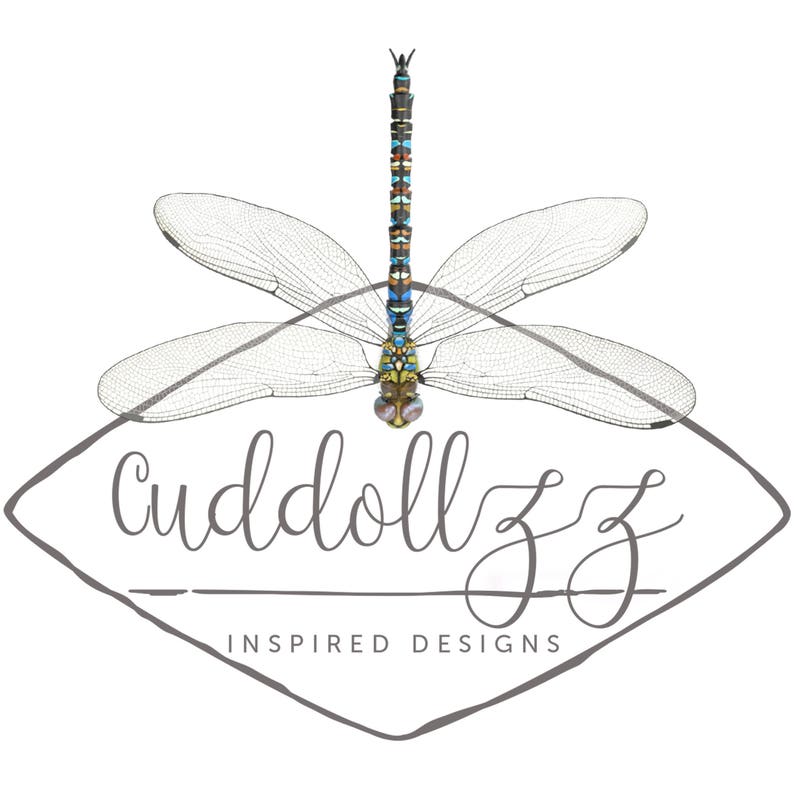 May include: A logo for a business called "cuddollzz inspired designs" featuring a stylized dragonfly with blue, green, yellow, and brown accents. The dragonfly is centered in a gray diamond shape.