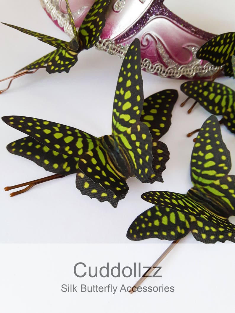 May include: Four green and black butterfly hair clips with gold wire accents. The butterflies have a spotted pattern. The text "Cuddollzz Silk Butterfly Accessories" is at the bottom of the image.
