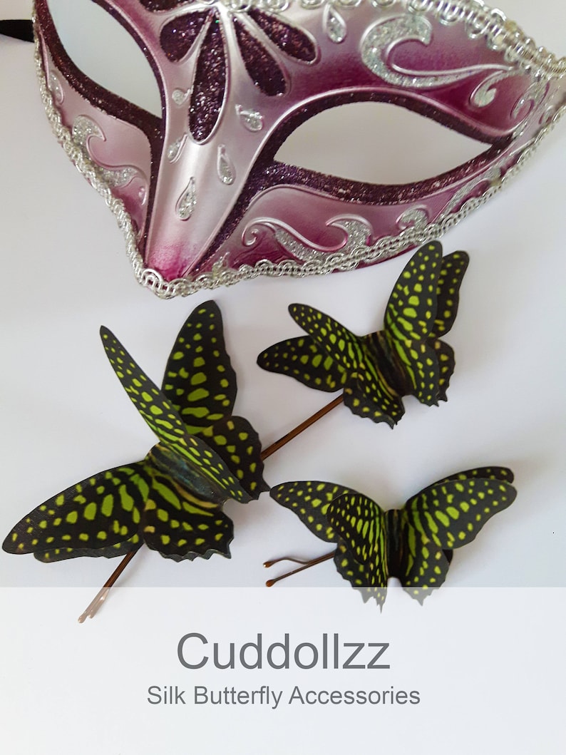 May include: Three green and black silk butterfly hair clips with gold wire stems. The butterflies have a spotted pattern. The image also includes a pink and silver masquerade mask.