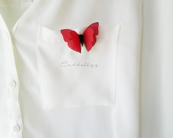 Peut inclure: Une chemise blanche à boutons avec une épingle en forme de papillon rouge dans la poche. Le texte "Cuddlezz" est écrit dans la poche.