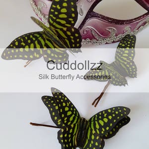 May include: Three green and black silk butterfly hair clips with brown wire stems. The butterflies have a spotted pattern. The text "Cudddollzz Silk Butterfly Accessories" is visible below the butterflies.