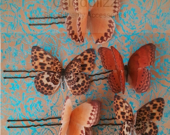 Puede incluir: Cinco pinzas para el pelo con forma de mariposa con alas marrones y naranjas. Las mariposas están hechas de tela y tienen un aspecto realista. Las pinzas están sujetas a horquillas.