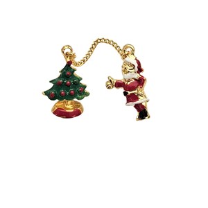 Può includere: Spilla a tema natalizio con un albero di Natale verde con ornamenti rossi e una figura di Babbo Natale in abito rosso con dettagli dorati. I due ciondoli sono collegati da una catena d'oro, su sfondo bianco.