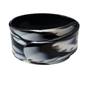 May include: A black and white marbled bangle bracelet. The bracelet has a rounded shape with a smooth, glossy finish. The design features swirling patterns of black and white, creating a unique and eye-catching accessory.