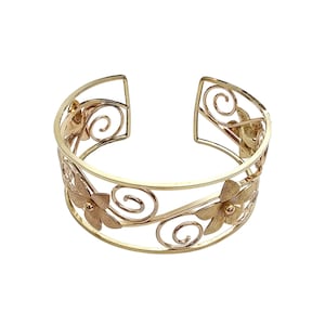 Puede incluir: Brazalete de puño dorado con diseño floral y de espirales. El brazalete abierto tiene una banda ancha con flores recortadas y detalles en espiral. El metal tiene un acabado pulido. Una pieza de joyería decorativa para cualquier ocasión.