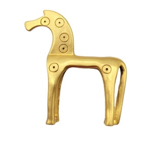 May include: A gold-colored metal horse figurine with a stylized design. The horse has a rounded head with five circular holes on the neck and two on the body.