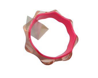 May include: A pink and beige silicone bracelet with a textured design. The bracelet is made of a soft, flexible material and has a smooth, rounded edge.